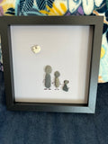 Handmade pebble art family shadow box with two adults and child holding hands beneath a heart