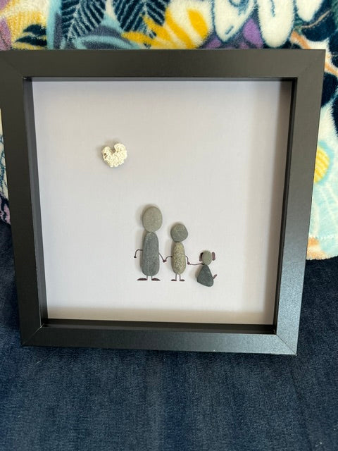 Handmade pebble art family shadow box with two adults and child holding hands beneath a heart