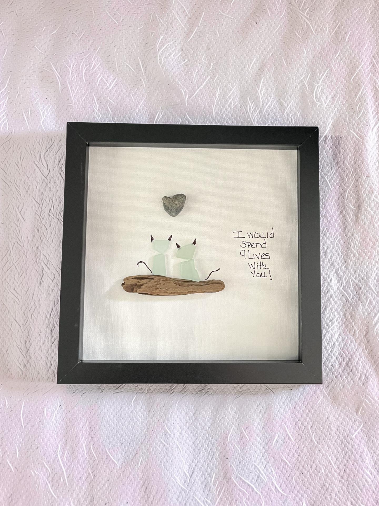 Two sea glass cats on driftwood with a beach stone heart and hand-lettered 9 Lives quote in a dark 8x8 shadow box frame